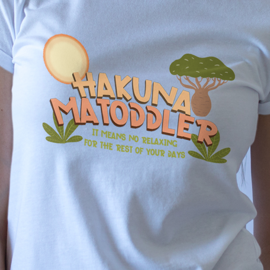 Woman wearing a white t-shirt with 'Hakuna Matoddler' graphic design on a light blue background